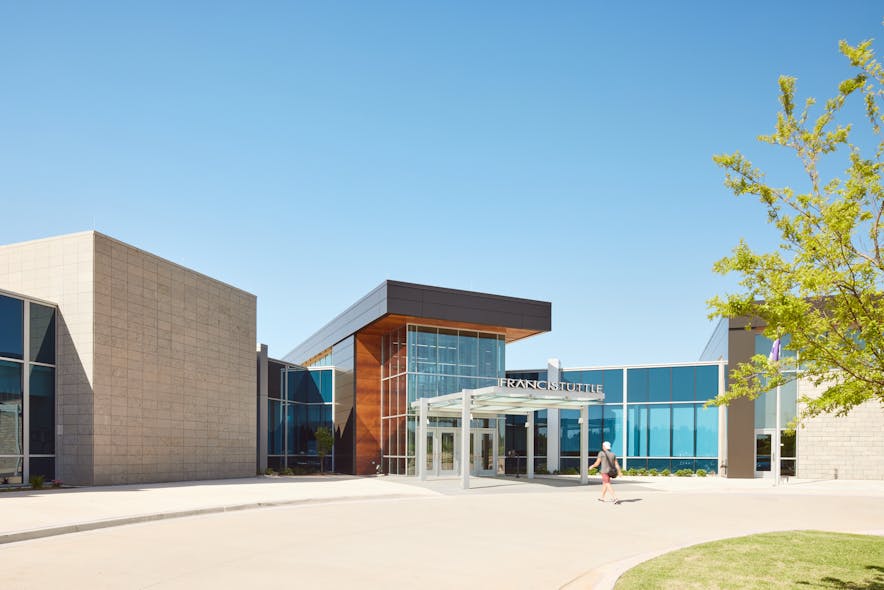 Students and visitors enter the building by walking under a glass canopy. The exterior landscape features mature trees and a fountain with the property nestled within a residential community in Oklahoma.