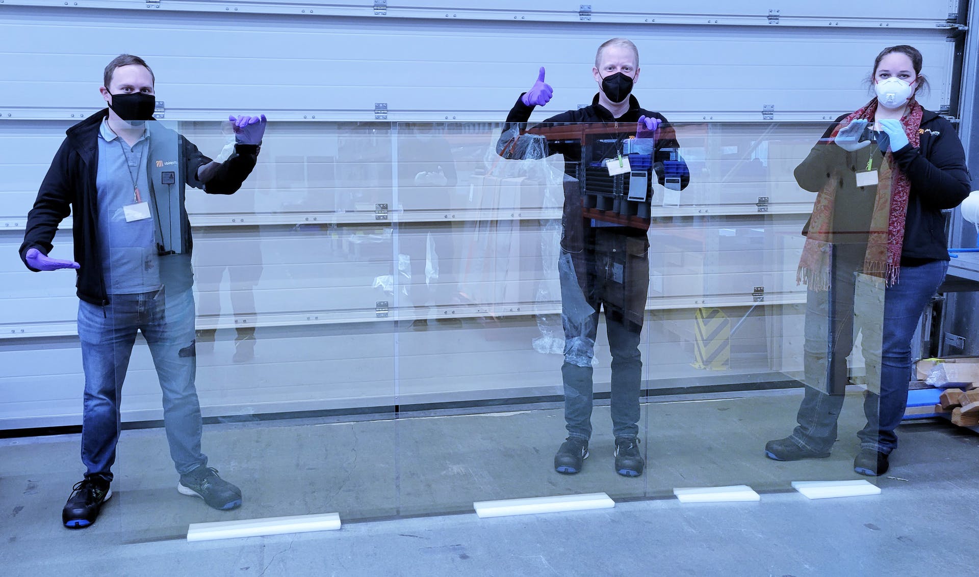 Ubiquitous Energy team holding 1.5 x 3.0 meter sized glass, coated with the company's UE Power transparent solar materials.