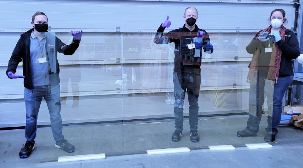 Ubiquitous Energy team holding 1.5 x 3.0 meter sized glass, coated with the company&apos;s UE Power transparent solar materials.