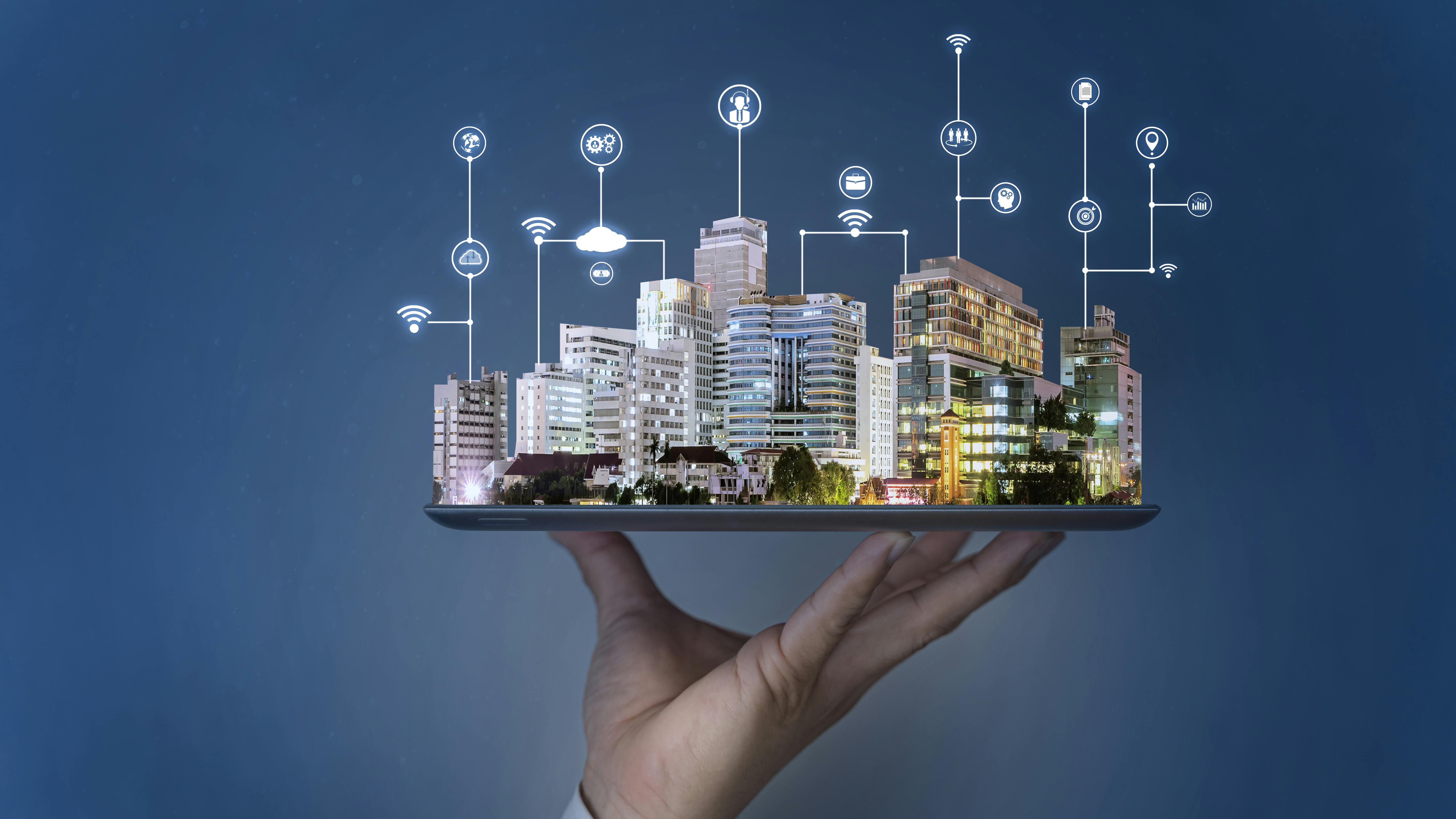 Image of human hand holding tablet with smart city projecting out of it.