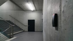 Concrete building stairwell with wall-mounted sensor in foreground and door in background. Concrete building stairwell with wall-mounted sensor in foreground and door in background.