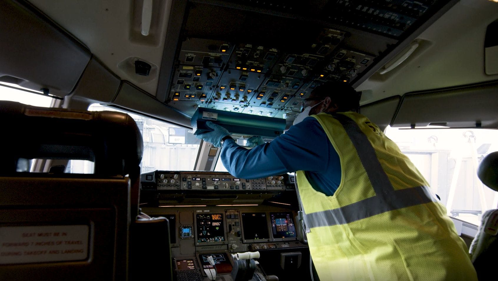 A worker in a United Airlines flight deck uses a handheld ultraviolet C-band (UV-C) device by American Ultraviolet to disinfect hard-to-clean control surfaces. The Cleveland Clinic consulted with the airline to evaluate the safety and efficacy of the process. (Photo credit: Screenshot from United Airlines B-roll video for media distribution.)