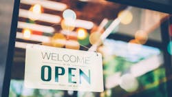 A sign reads 'Welcome We Are Open' in a glass storefront window. A sign reads 'Welcome We Are Open' in a glass storefront window.