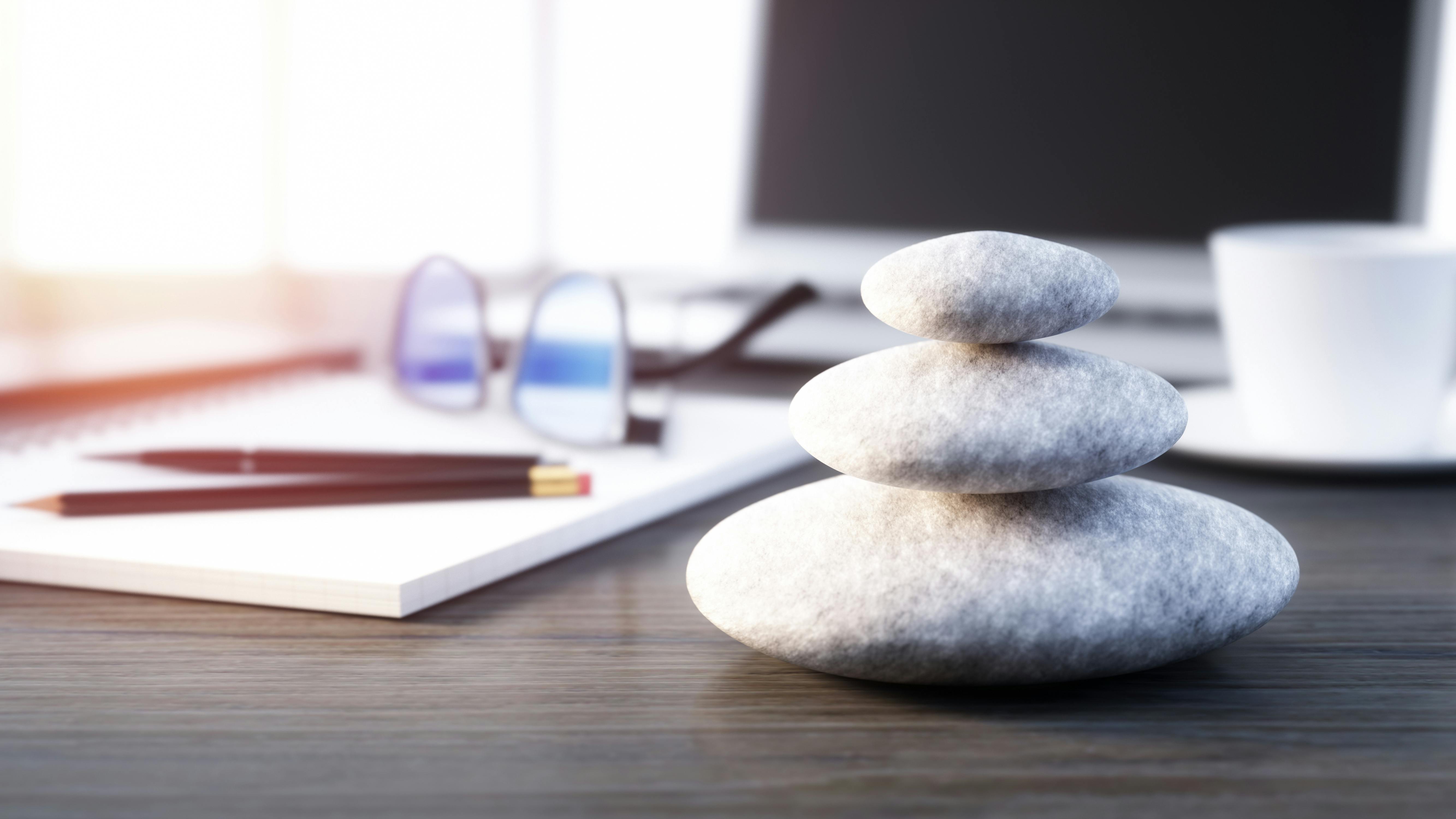Stack of smooth stones on desktop in front of laptop computer with pad of paper and pencil on the side