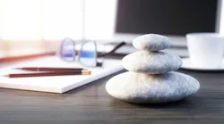 Stack of smooth stones on desktop in front of laptop computer with pad of paper and pencil on the side