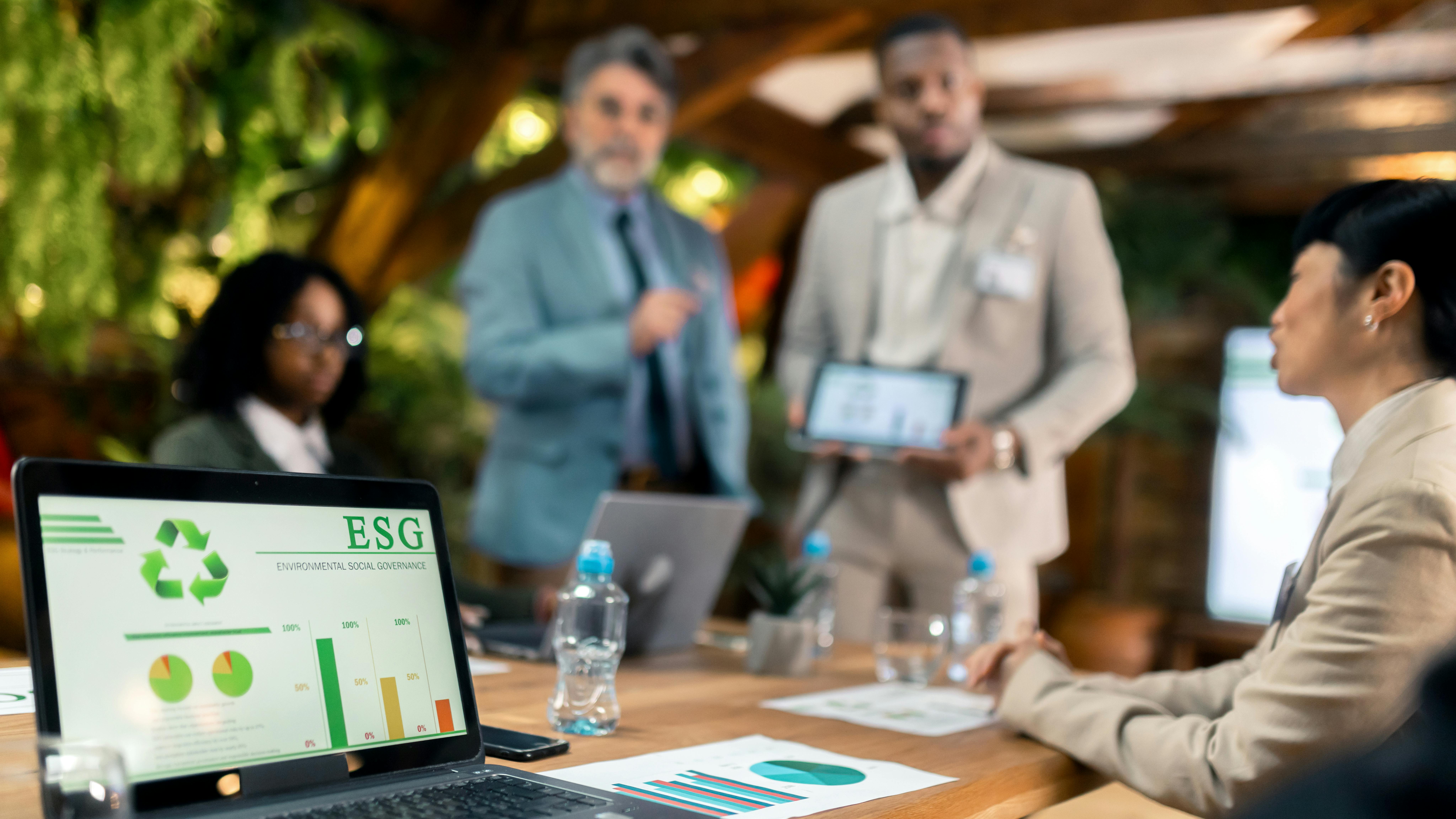 Group of employees around conference table with laptop open to ESG screen.