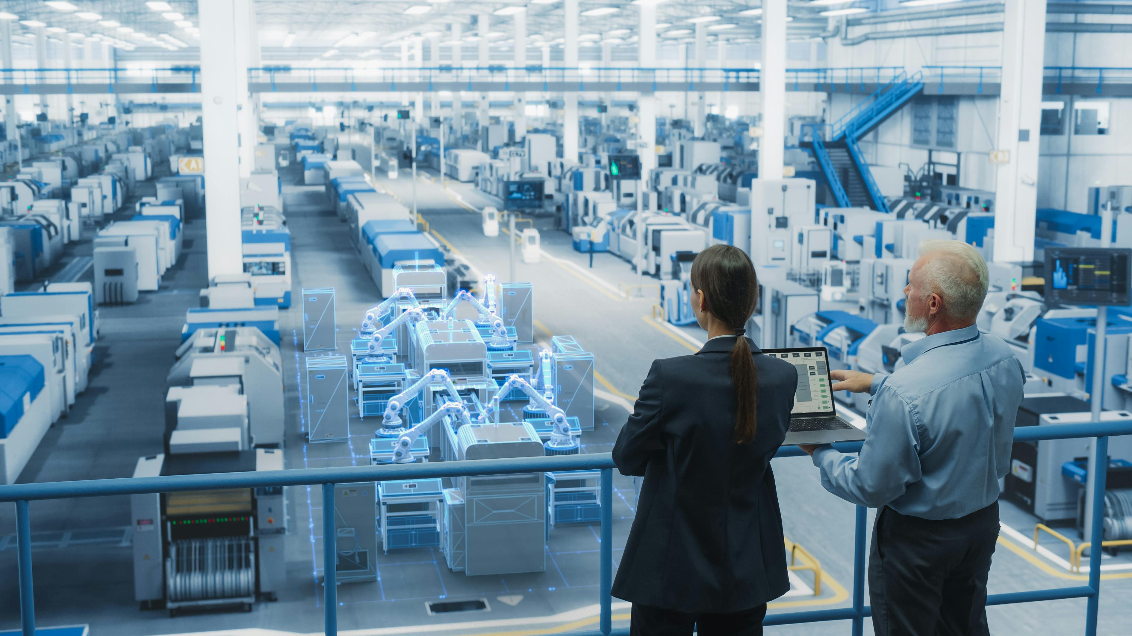 Man and woman stand above modern manufacturing facility floor with laptop in hand.