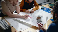 A Dreamstime image of three people working around a table that has site plans and product samples set out.